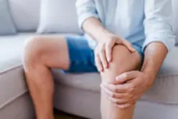 man holds knee in pain from osteoarthritis