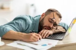 A man struggles to stay awake at work and wonders “Is chronic fatigue syndrome considered a disability?”