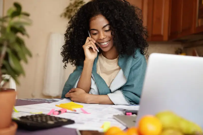 A young black woman sits at a desk on the phone. She is happy because she just got legal funding from Rockpoint Legal Funding, the best pre-settlement funding company for lawsuit loans.