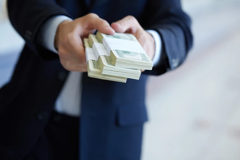 Man in suit handing over post-settlement funding cash