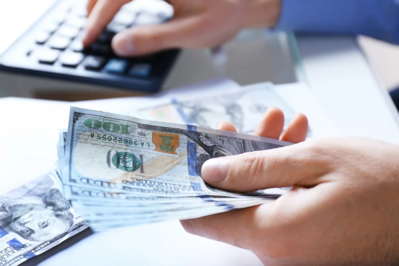 Man holding Legal Funding money on left hand and using calculator with right hand