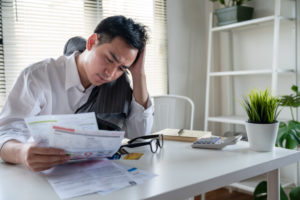 A young man holds bills in his hands looking visibly stressed out.