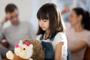 A girl sits with her stuffed toy while her parents sit nearby behind her. You can consult with a child custody lawyer to determine when you can terminate a non-custodial parent's rights in Georgia.