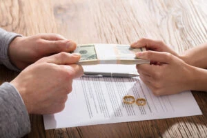 A couple holds a stack of money over a piece of paper and their wedding rings. You can consult with a lawyer who can represent you in a high net worth divorce.