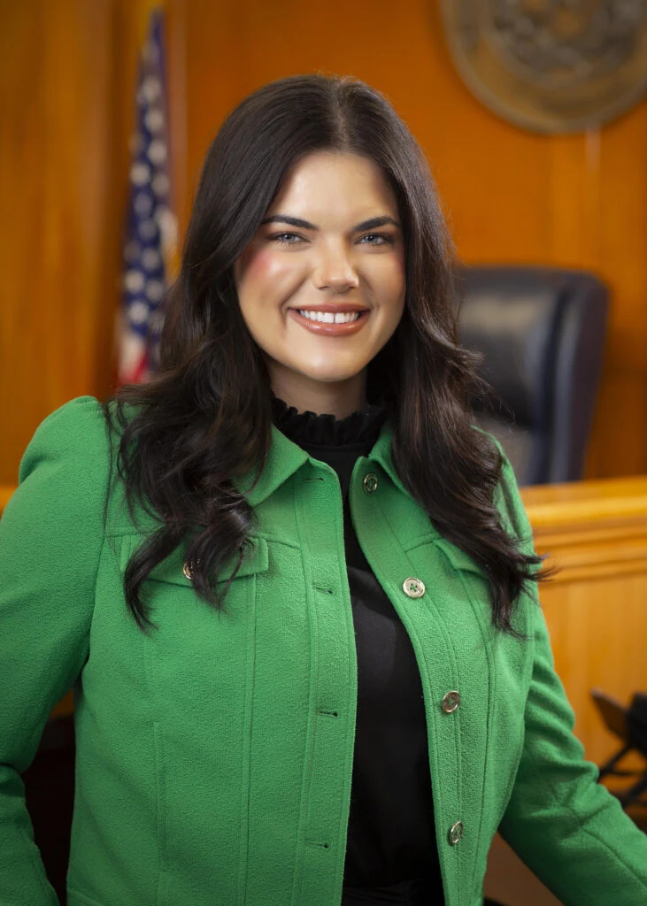 Smiling woman in a green jacket inside the court room.
