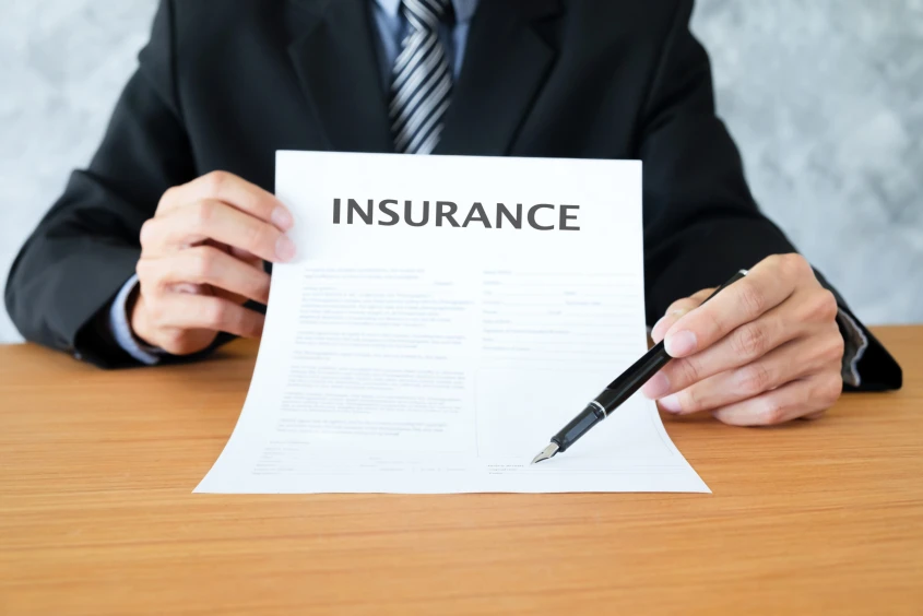 A young man in suit in his office showing an insurance policy and pointing with a pen where the policyholder must sign.