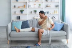 a-man-sitting-on-a-couch-with-crutches-and-his-leg-in-a-cast-after-suffering-a-personal-injury