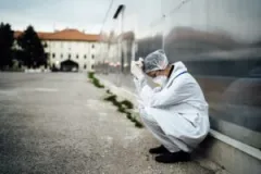 doctor in white scrubs leans up against building crying ptsd