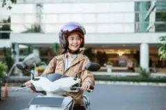 A young woman smiles while riding a motorcycle.