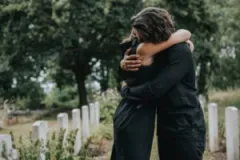 A grieving couple hug in a cemetery.