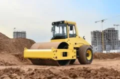 A yellow soil compactor sits unused at a worksite.