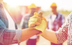 Two construction workers grasp hands in front of an out-of-focus team