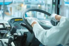 A gloved, faceless bus driver navigates through city traffic.