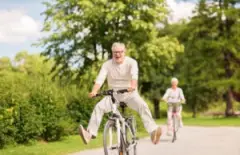 An older couple happily bicycles down a country lane on a sunny day.