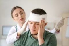 A man with a head injury that qualifies as a traumatic brain injury is getting his head bandaged by a nurse.