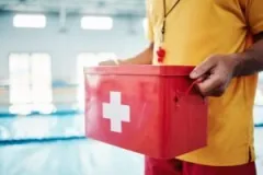 A lifeguard carries a box with medical supplies to a drowning accident victim at an indoor swimming pool. A drowning accident lawyer can help the victim seek compensation.