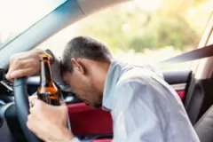 A man with a bottle in hand passes out at the wheel of a car.