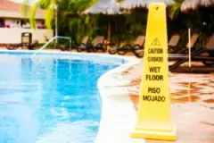A bright yellow caution sign stands by a pool.