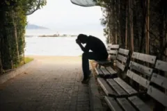 A shadowed young man sits on a bench and grieves the loss of a loved one.