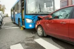 A red car collides with the front of a bus on a city street.
