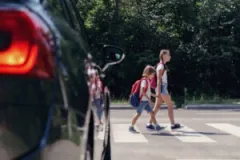 Two children crossing the road in front of a vehicle. After a crash, you can reach out to a Portage pedestrian accident lawyer.