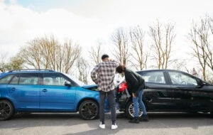 Two people looking at a vehicle after a crash and wondering what happens if your rideshare driver is in an accident.