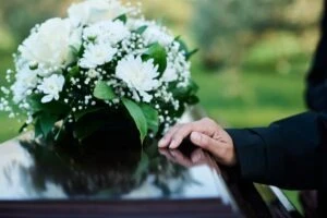 A woman standing by a coffin at a funeral and wondering if you can sue if your spouse died at work.