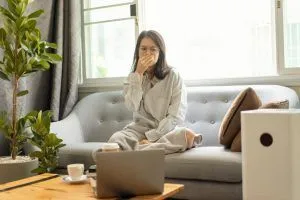 A woman sits on her couch, covering her face
