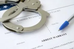 District Court Arrest Warrant court papers with handcuffs and blue pen on United States flag.
