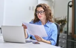 Young busy business woman manager, lawyer or company employee holding accounting bookkeeping documents checking financial data or marketing report working in office with laptop.