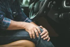 A driver holds his injured knee after a car crash. The most common leg injuries after a car accident include broken bones and lacerations. A personal injury lawyer will fight to recover your medical bills.