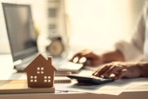 Wooden house carving in the foreground with a Texas real estate broker using a computer and calculator in the background