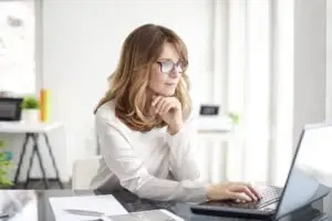 A businesswoman with glasses is sitting in front of a laptop.