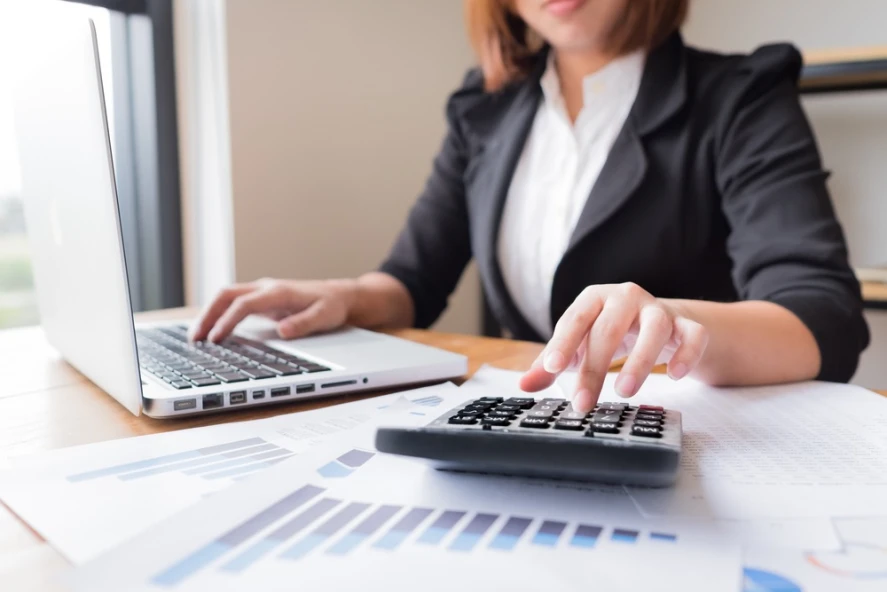 An accountant uses a calculator and computer to work at her desk.