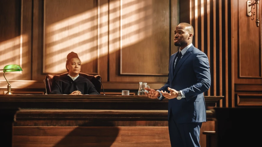 a man stands in a courtroom before a judge to deliver expert witness testimony