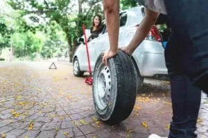man pushing spare tire up to Asian woman’s car