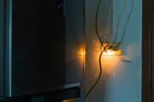 fiery electric plug behind a refrigerator