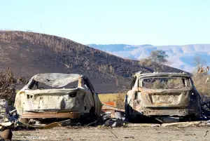 Two cars parked off the road, burned in the North Bay firestorm. Charred landscape in the background.