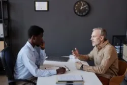 An older male sits with a younger boss at desk – thinks how to prove age discrimination.