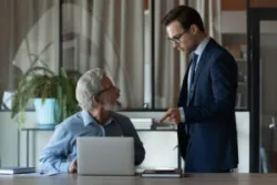 An angry boss scolds a senior employee, pointing a finger at the laptop screen, displaying age discrimination at work.