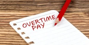 The words "overtime pay" are written in red pencil on a piece of paper. If Walmart has not paid you for the overtime you worked, consult an employment and labor lawyer who can file a complaint and take legal action to recover your wages.