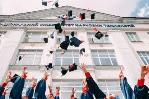 graduates throwing caps into the air in front of college