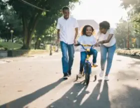 mom and dad teaching child how to ride a bicycle