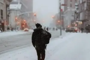 pedestrian wearing winter coat & hat walking down the street