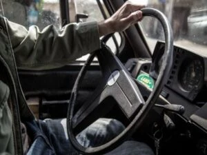 A man's left hand resting on the steering wheel of a truck.