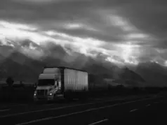 black & white image of semi-truck driving with clouds in the background