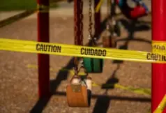 Empty saddle style swings at a playground covered in yellow caution tape written in english and spanish