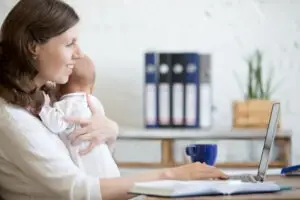 Woman holds newborn and uses computer while on maternity leave of absence