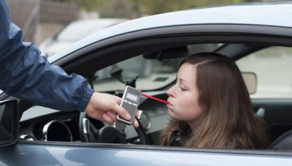 Woman being breathalyzed at a road sobriety stop in her car with a police officer