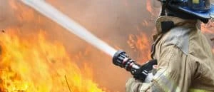 Firefighter spraying a hose towards a raging fire